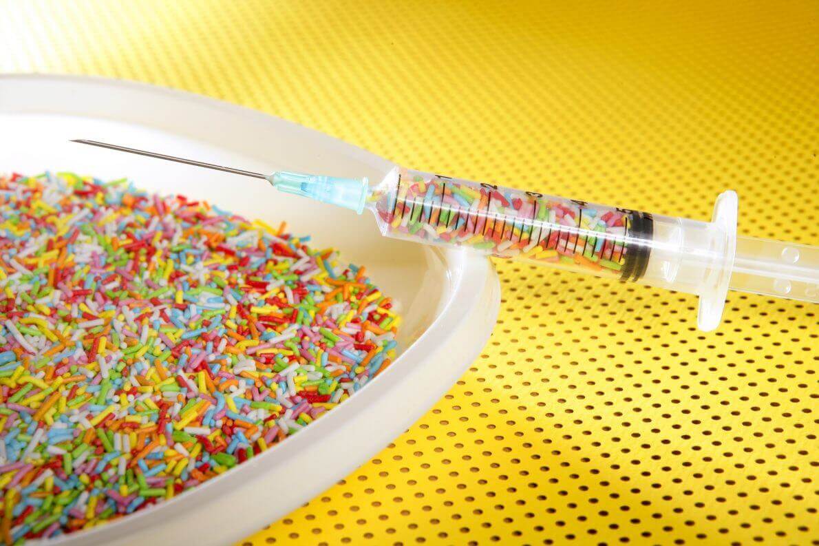 Little colorful candy syringe over yellow background